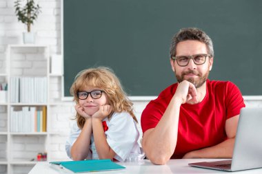 Eğitim ve öğrenme kavramı. İlkokul öğrencisinin dersi var. Öğretmeni olan çocuk İngilizce ya da matematik öğreniyor. Baba ve oğul okulda ödev yapıyor.