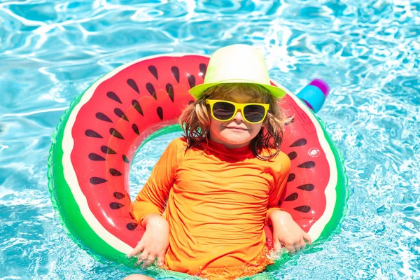 Child swim in summer pool water. Kid in swimming pool, relax swim on inflatable ring and has fun in water on summer vacation