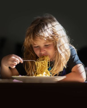 Küçük çocuk mutfakta spagetti yiyor. Şirin çocuk kaşıkla yemek yiyor. Küçük çocuk yemek yiyor, yakın plan çocuk yüzü. Makarna yiyen komik bir çocuğun portresi.
