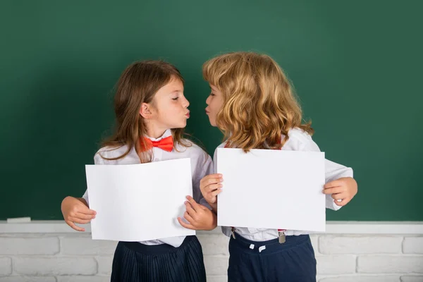 Kids love, first kiss. Back to school. Schoolchild friends back to school at knowledge day. Schoolkids holding white paper blank, poster with copy space