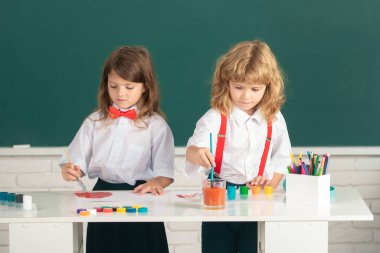 Çocukların yaratıcı gelişimi. Okulda resim çizen ve resim yapan sevimli okul arkadaşları. Dost canlısı bir oğlan ve komik öğrenciler çizer. Okulda arkadaşlık.