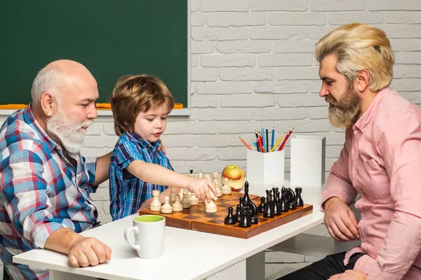 Grandfather father and son playing chess. Grandpa teaching grangson at school class. Man generation concept