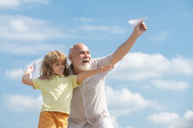 Büyükbaba ve oğlu, kağıt uçakla yaz aylarında arka planda oynuyorlar. Uçma ya da seyahat hayali kuran çocuk.