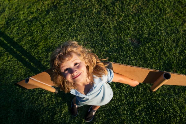 芝生の夏の丘の外の空の背景におもちゃの飛行機で遊んでいる白人の子供 幸せな未来のコンセプトを夢見て — ストック写真