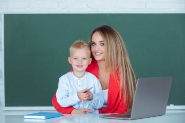 İlkokul öğretmeni ve öğrenci sınıfta. Anne ve oğlu birlikte bilgisayar laptopu kullanıyorlar.