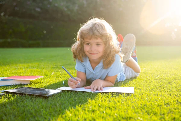 Cute childr boy writing notes in copybook outdoors. Summer camp. Kids learning and education concept