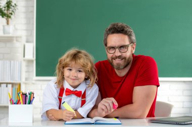 Okula dönelim. Çocuk öğretmenden öğreniyor. Sınıfta babasıyla tahtada ders çalışan komik küçük çocuk. İlkokuldan bir çocuk