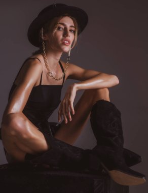 Siyah yuvarlak şapkalı şık giyinmiş bir kadın. Moda kıyafeti giyen çekici, şehvetli, genç bir bayanın moda portresi.