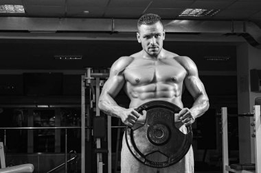 Spor salonunda ağırlık diski olan bir Powerlifter. Ağır diski olan vücut geliştirici pazılarını çalıştırıyor.