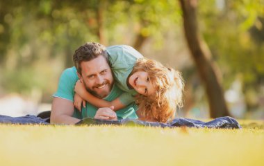 Baba ve çocuk dışarıda kucaklaşıp sarılıyorlar. Baba ve oğul yaz parkında çimlere uzanmış dışarıda vakit geçiriyorlar.