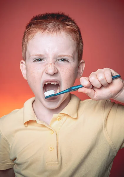Cute funny boy with a toothbrush. Happy little boy brushing his teeth. Adorable little boy holding toothbrush and smiling at camera isolated on red. Dental hygiene