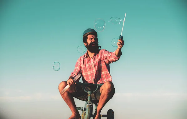 Funny man on a bicycle. Emotional crazy guy on a childrens bike. Funny young man with motorbike helmet, poses on bike, wears shirt. People, transportation and riding concept