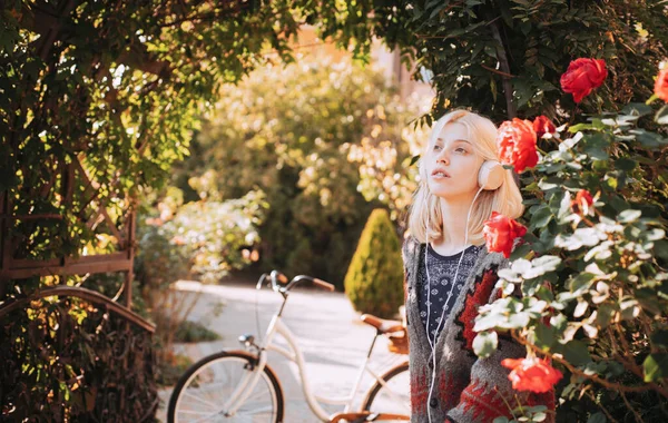 Active girl with headphones. Favorite music. Woman headphones blooming garden. Weekend activity. Active leisure and lifestyle. Girl listen music and ride bicycle. Blonde enjoy music in park or garden.
