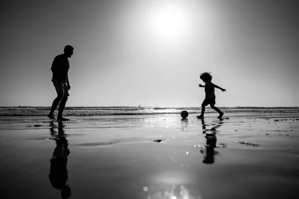 父亲和儿子在海滩上踢足球或踢足球 爸爸和孩子在户外玩耍 日落时的轮廓 积极的家庭概念 — 图库照片