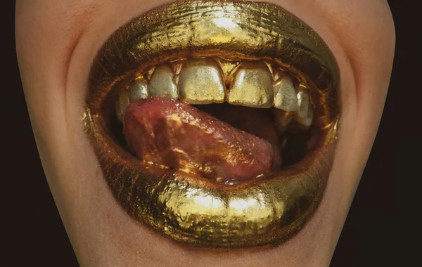 Gold paint on lips. Golden lips, sensual woman mouth. Metallic creative art make up close up. Gold concept. Sexy tongue. Sensual lick