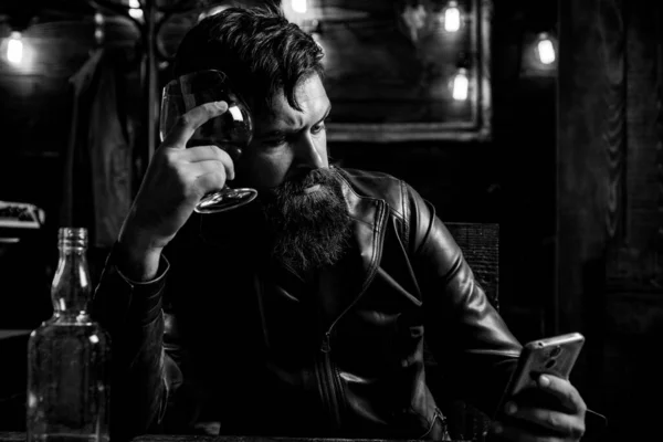 残忍的嬉皮士人喝酒 英俊英俊英俊的大胡子男人喜欢威士忌和做他的生意在Smatphone 穿着皮夹克的优雅男子在酒吧喝威士忌 — 图库照片