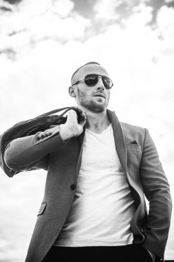 Bayım. Mükemmellik. Takım elbiseli, güneş gözlüklü ve bulutlu gökyüzüne bakarken yüzünü çeviren yakışıklı genç adamın yakın çekimi. Adam bulunmaya hazır. Yeni bir hayatın beklentisiyle