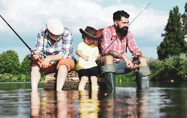 Boy with father and grandfather fly fishing outdoor over river background. Young - adult concept. Old and young. Little boy on a lake with his father and grandfather