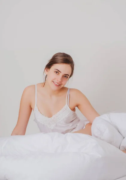 Young woman in the morning after good sleep in white comfortable bed, girl lying on soft pillows awaken in cozy bedroom, morning relaxation concept