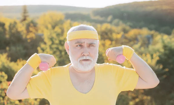 Grandfather exercising with dumbbell. Sport for senior man. Senior man in park working out with weights