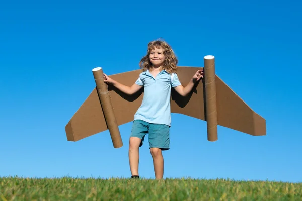 青い空に対しておもちゃの飛行機の段ボールの翼で幸せな子供の遊び 夏の野外で楽しんでいる子供 紙翼を持つ少年の肖像 — ストック写真