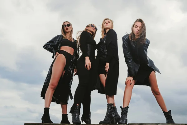 Fashion portrait of group fashion models girls posing outdoor, black style outfit against sky. Attractive young vogue women. Group of multi-ethnic friends