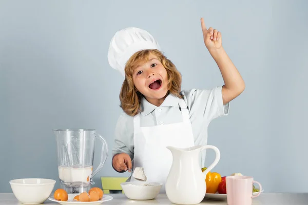 Child wearing cooker uniform and chef hat preparing food with flour on kitchen, studio portrait. Cooking, culinary and kids food concept