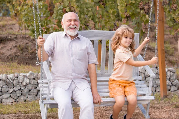 Grandfather and son swinging in garden. Granddad and grandchild playing on swing