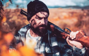 Ormanda kaçak avcı. Sakallı avcı silah tutuyor ve ormanda yürüyor. Av ruhsatı. Avlanan av tüfekli avcı