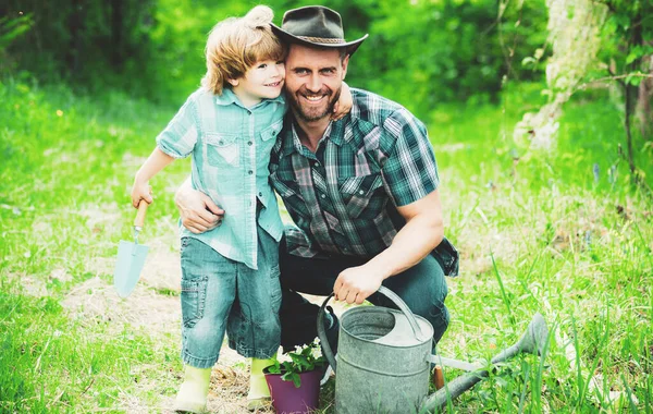 Dad and son spending free time together in garden and hugging. Son helping his father to plant the tree while working together in the garden. Smiling face. spring time