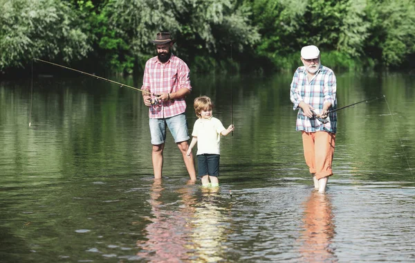 ひいおじいちゃんとひ孫湖で釣りをする父と祖父の孫 川のバースに釣り竿を持つ幸せな祖父 父と孫 — ストック写真