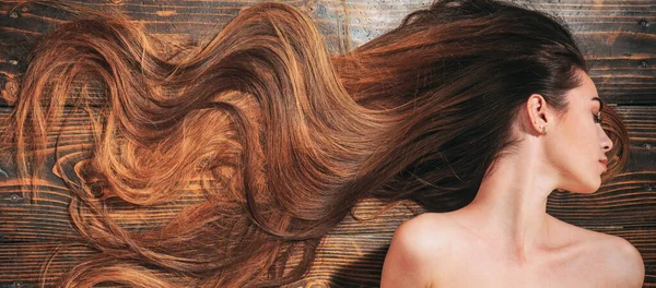 Very long hair on wooden background. Beautiful model with curly hairstyle. Hair Salon concept. Care and hair products