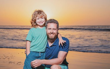 Baba oğul kumsalda gün batımında sarılıyorlar. Küçük oğlum, gün doğumunda babanı kucakla.