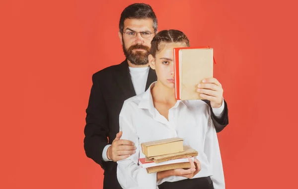 Portrait of teacher and young student. Modern attractive teacher. Portrait of young schoolgirl with book isolated on the red background. Study concept