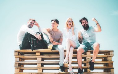 Arkadaşlardan oluşan öğrenciler sınavları geçtikten sonra mutlu hissediyorlar. Çılgın sakallı adam ve sarışın kadın. Açık gökyüzü arka planında bankta oturan dört arkadaş grubu