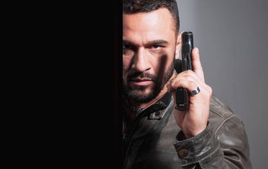 Elinde silah tutan bir adamın portresi. Yakışıklı sakallı adam. Tehlike. Geçmişi karanlık olan bir tetikçi. Ciddi stil sahibi sakallı adam. Ciddi yüzlü ve acımasız bir adam.