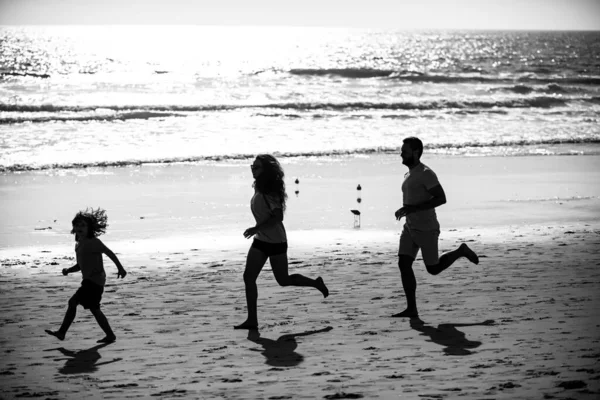 Silhouettes of family jogging along sea beach at sunrise. Outdoor workout, silhouettes of runners, sport and healthy family lifestyle