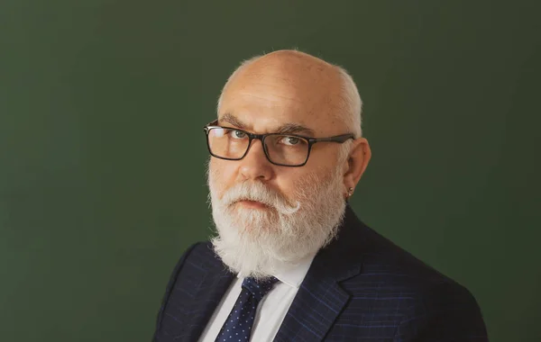 Serious teacher. Closeup portrait of senior academic professor near empty blackboard. Knowledge and traditional education concept