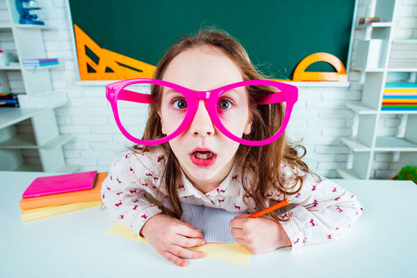 Funny geek surprised child school girl with fun glasses in classroom. Back to school