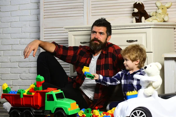 Father and son create toys from bricks. Cute little kid son play toy cars with dad, happy family son and loving young father babysitter having funon floor at home. Dad and kid build of plastic blocks