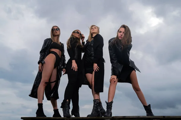Fashion portrait of group fashion models girls posing outdoor, black style outfit against sky. Attractive young vogue women. Multiethnic group of young models in black
