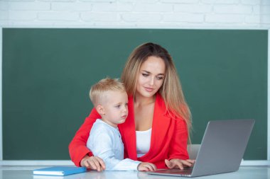 Anne ve oğul öğreniyor. Öğretmen okulda okul çocuğuna yardım ediyor. Küçük okul çocuğu annesiyle dizüstü bilgisayar kullanıyor.