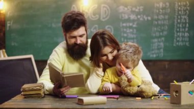 Cute clever boy study. Young mother father and little preschooler boy sit at table drawing together, playing, painting pictures in notebook, early development