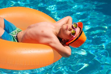 Çocuklar yaz tatilinde yüzme yüzüğüyle yüzerler. Çocuk havuzda su sıçratıyor, eğleniyor, boş vakit geçiriyor.