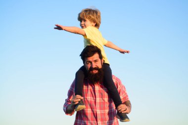 Mutlu bir aile. Çocuk evlat babasına gökyüzüne karşı sarılıyor. Aile tatili, babalar günü. Babası onu omuzlarında taşırken mutlu küçük çocuk ellerini uzatıyor.