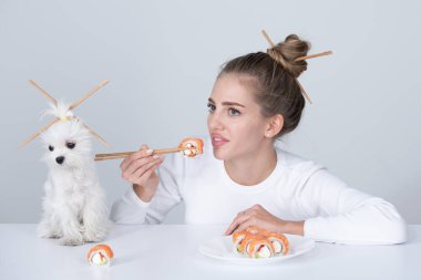 Japon kadın suşi stili. Japon suşi seti yiyorum. Güzel genç kadın ve köpek yemek çubuklarıyla suşi yiyorlar, beyazın üzerinde izole edilmiş. Çubuklu suşi. Sağlıklı Japon yemekleri