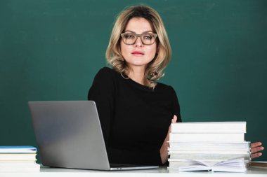 Sensual student woman in eyeglasses near blackboard. Sexy beautiful girl sit on table on chalkboard. Attractive female teacher in college