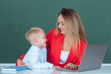 Anne ve oğlu birlikte bilgisayar laptopu kullanıyorlar. İlkokul sınıfı. Sınıfta öğretmen ve öğrenci. Öğretmen genç öğrencilere dizüstü bilgisayar kullanıyor.