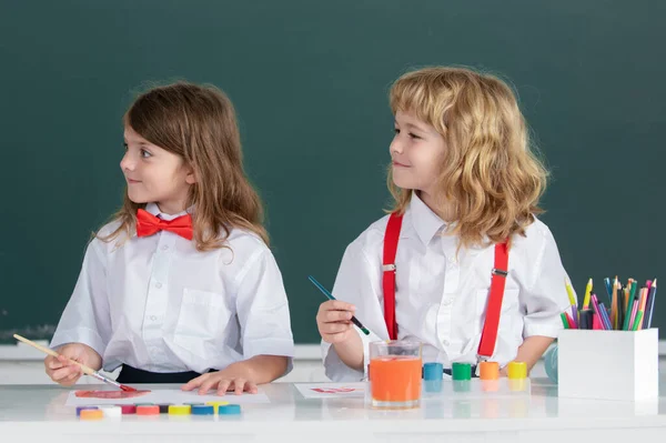 Cute school friends kids drawing and painting at school. Friendly boy an girl funny pupils draw. Friendship in school. Kids creative education