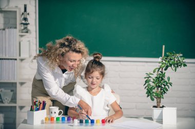 Kid drawing with teacher. Children from elementary school study at draw lesson. Pupil with teacher painting. Education and knowledge